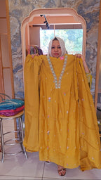 Woman holding a yellow dress with intricate designs in front of a mirror.